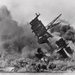 The battleship USS Arizona belches smoke as it topples over into